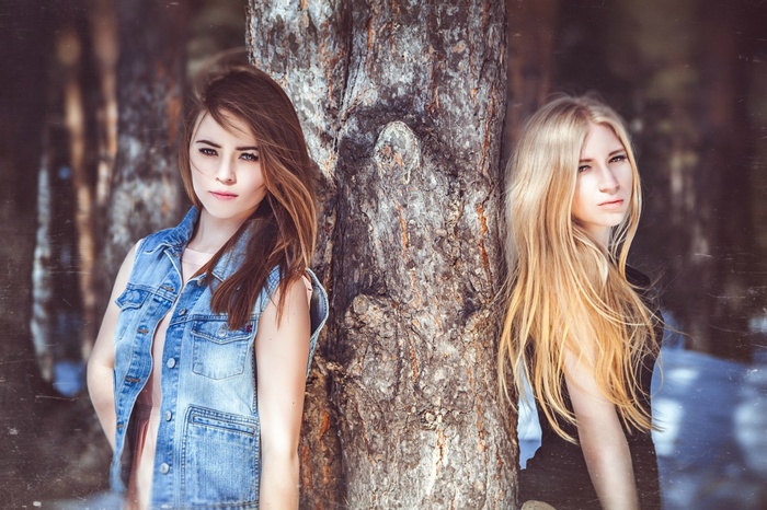 Two women leaning against a tree in a forest
