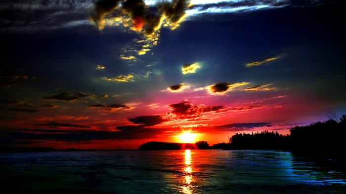 Dramatic sunset over a body of water with silhouetted trees