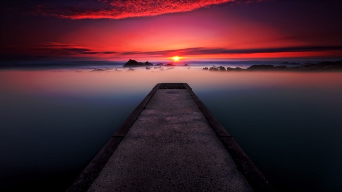 Concrete pier leading to a misty sunset over the ocean