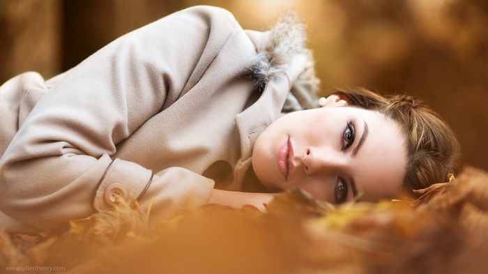 Woman in a white coat lying on autumn leaves