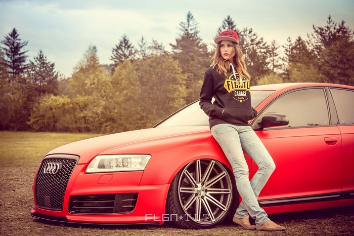 Woman in hoodie and cap leaning on red Audi A6