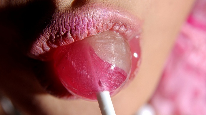 Woman with pink lipstick licking a lollipop
