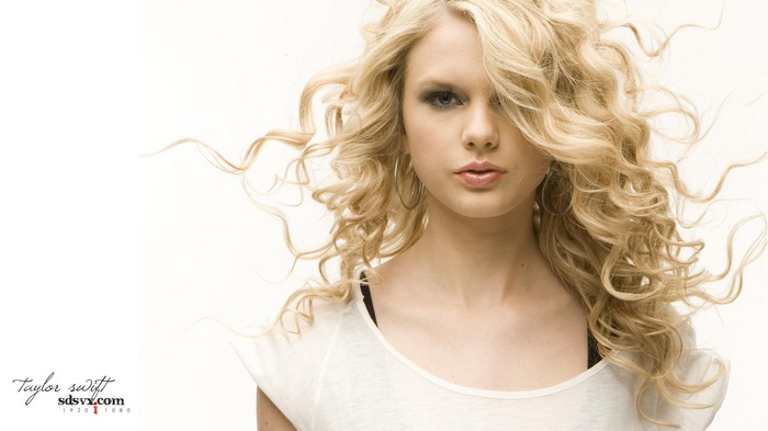 Taylor Swift with curly blonde hair and hoop earrings