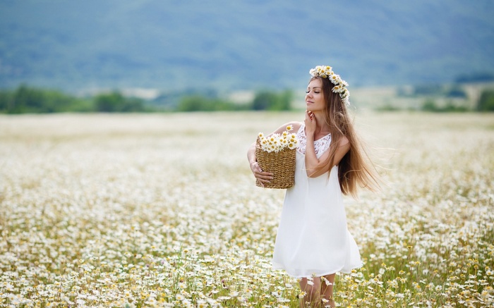 Woman with chamomile crown and basket in a field