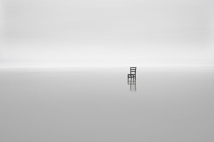 Minimalist monochrome image of a chair on a reflective surface
