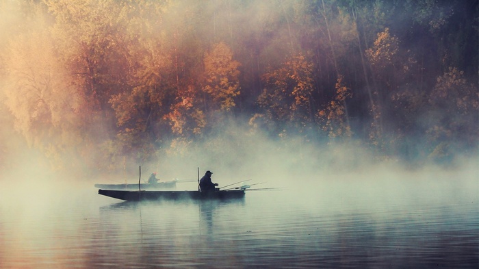 Fishermen in boats on a misty lake at sunrise