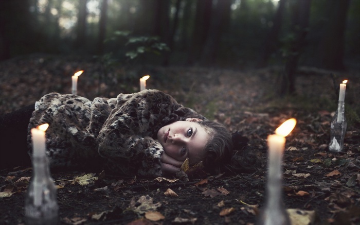 Woman lying in a forest with candles