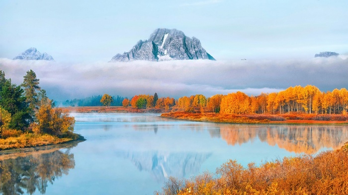 Autumn trees reflected in a misty river with mountains