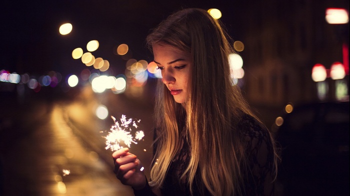 Woman holding a sparkler at night with bokeh lights