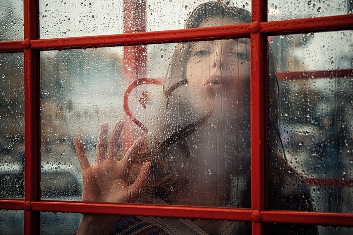 Woman drawing heart on rainy window