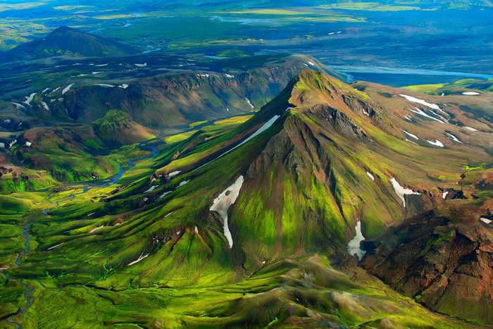 Aerial view of Iceland's green mountains with snow and rivers