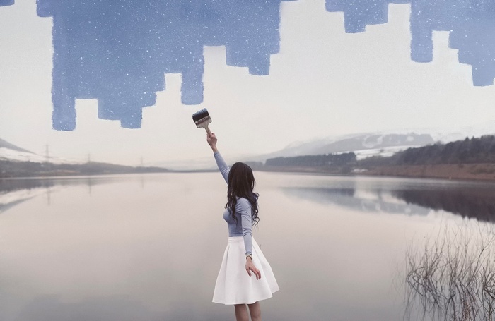 Woman painting a cityscape over a lake landscape
