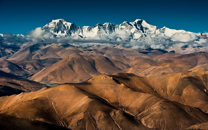 Snow-capped mountains above brown hills under a blue sky