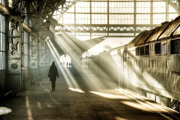 Sunbeams illuminate a train station with a lone figure walking