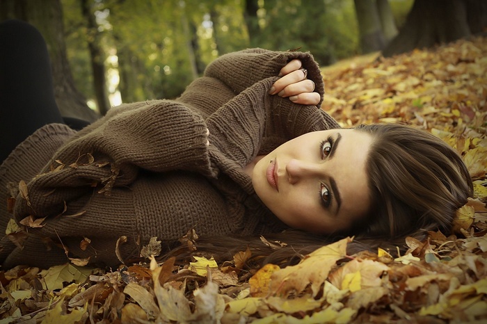 Sandra lying in autumn leaves wearing a brown sweater