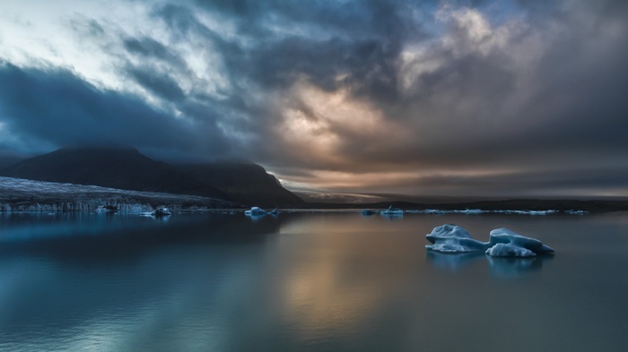 Icebergs floating in a lake with mountains and clouds