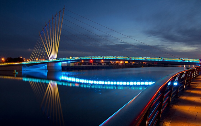 Bridge illuminated at night over a river with reflections