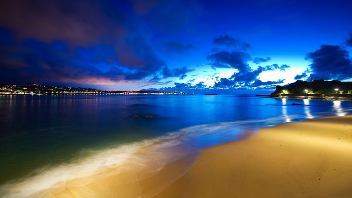 Beach at night with city lights and ocean waves
