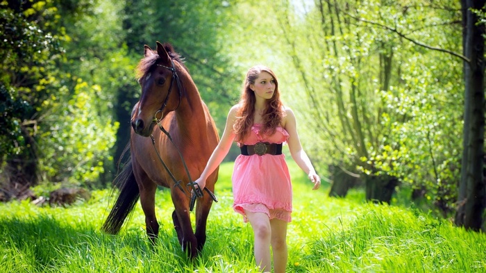 Woman in pink dress walking with a horse in nature