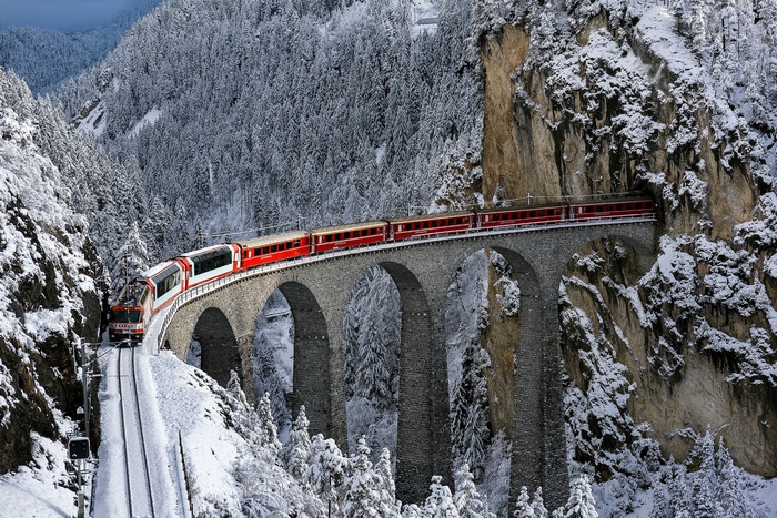 Red train crossing a snowy viaduct in Switzerland