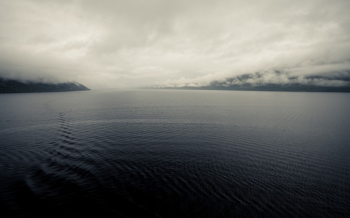 Misty lake with forested shores and cloudy sky