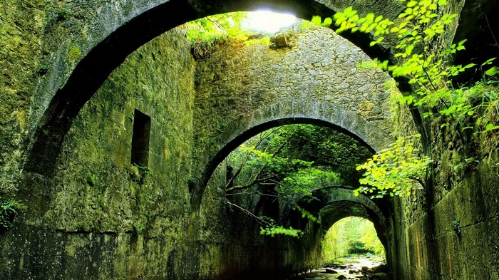 Moss-covered stone arches over a stream with sunlight