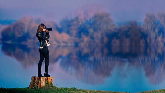 Woman with camera on stump by lake with reflections