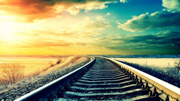 Railroad tracks curve towards a colorful sunset sky