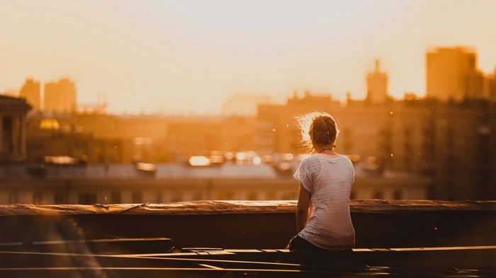 Woman sitting on a rooftop at sunset overlooking city