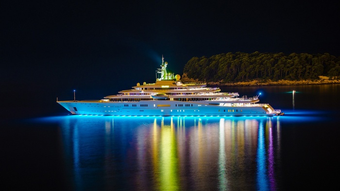 A large yacht illuminated at night with reflections on the water