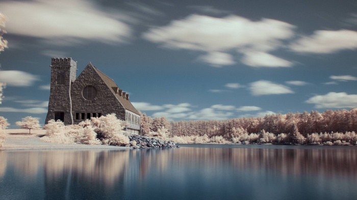 Stone building by a calm lake with white trees and clouds