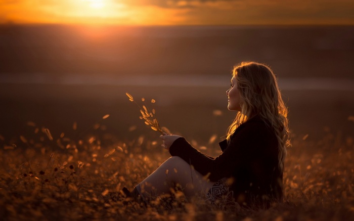 Woman sitting in a field at sunset