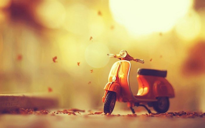 Orange toy Vespa scooter with fall leaves