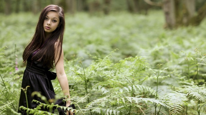 Woman with long hair in a black dress in a fern field