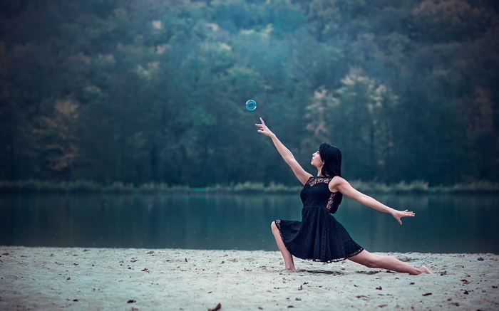 Woman in black dress playing with bubbles by the water