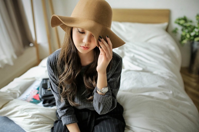 Asian woman with long hair wearing a hat sitting on a bed