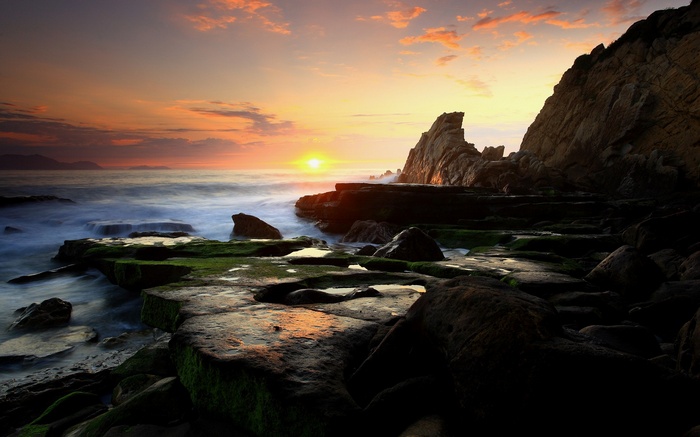 Sunset over rocky coast with waves crashing