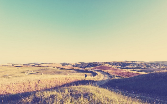 Rolling hills with haystacks and a winding road