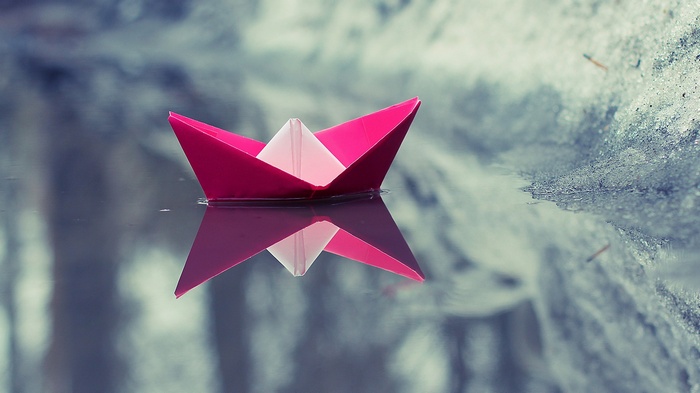 Pink origami boat floating on water with reflection
