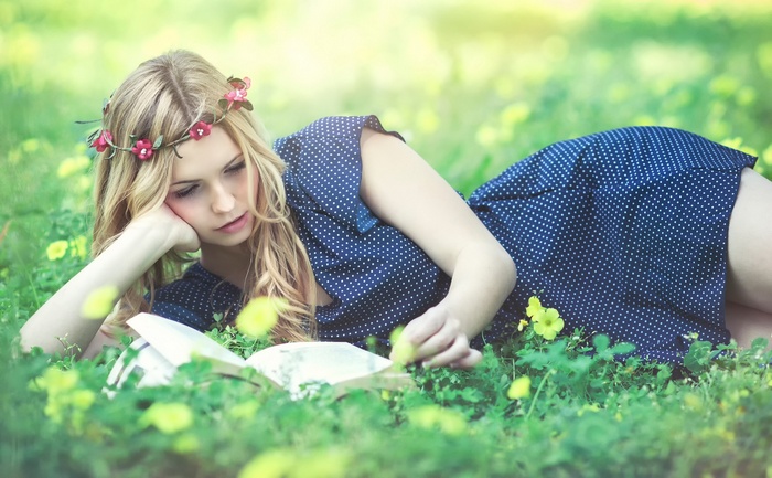 Woman with flower crown reading a book in grass
