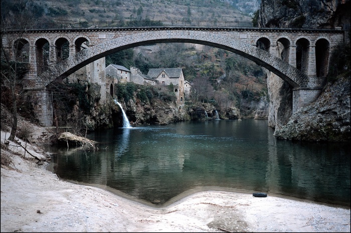 Stone bridge over a river with waterfalls and a village