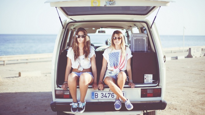 Two women in jean shorts sitting in the back of a Volkswagen van at the beach