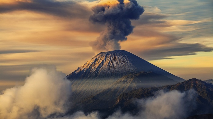Volcano erupting smoke into the sky with clouds