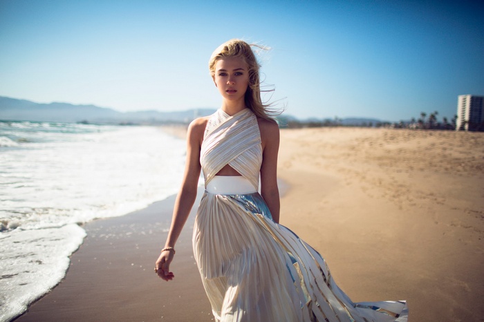 Nicola Peltz walks on the beach in a flowing dress