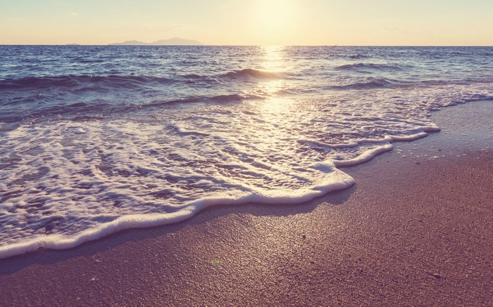Ocean waves washing onto a sandy beach at sunset