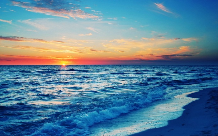 Sunset over the ocean with waves crashing on the beach