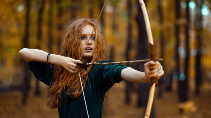 Redhead woman aiming a bow and arrow in a forest
