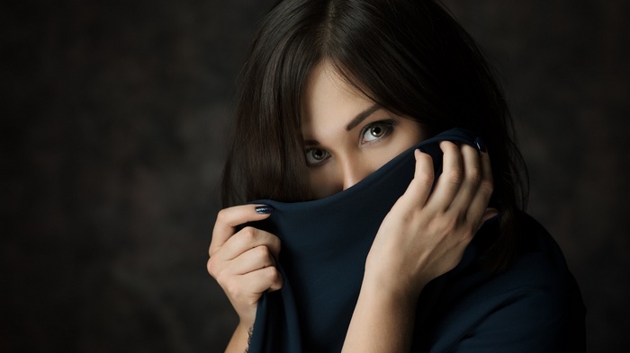 Woman with dark hair and green eyes covering face with fabric