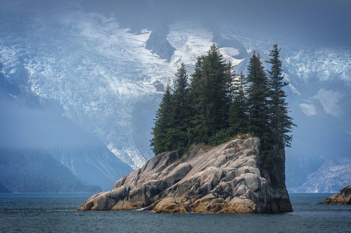 Rocky island with pine trees and snowy mountains
