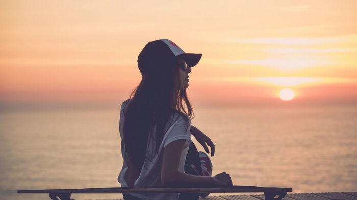 Woman in cap sitting on a skateboard at sunset